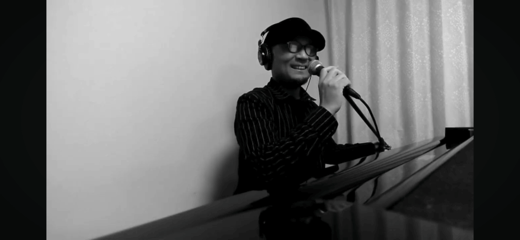 ピアノを弾きながらマイクで歌う男性ジャズミュージシャンのモノクロ写真:日本では珍しい弾き語りスタイル